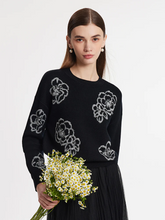 a lady wearing a black floral jacquard round neck sweater